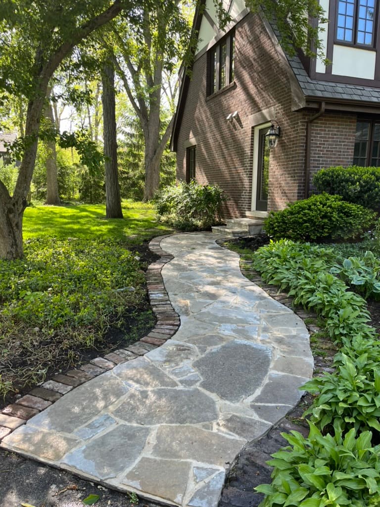 Winding natural flagstone path with brick edging through shaded garden