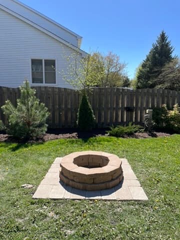 Two-tier stone fire pit with square paver base and landscape integration